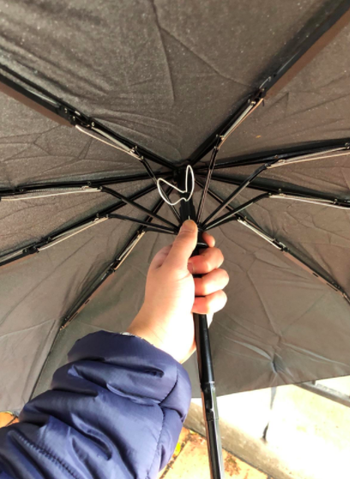 Reviewer shows inside of gray windproof umbrella while walking outside