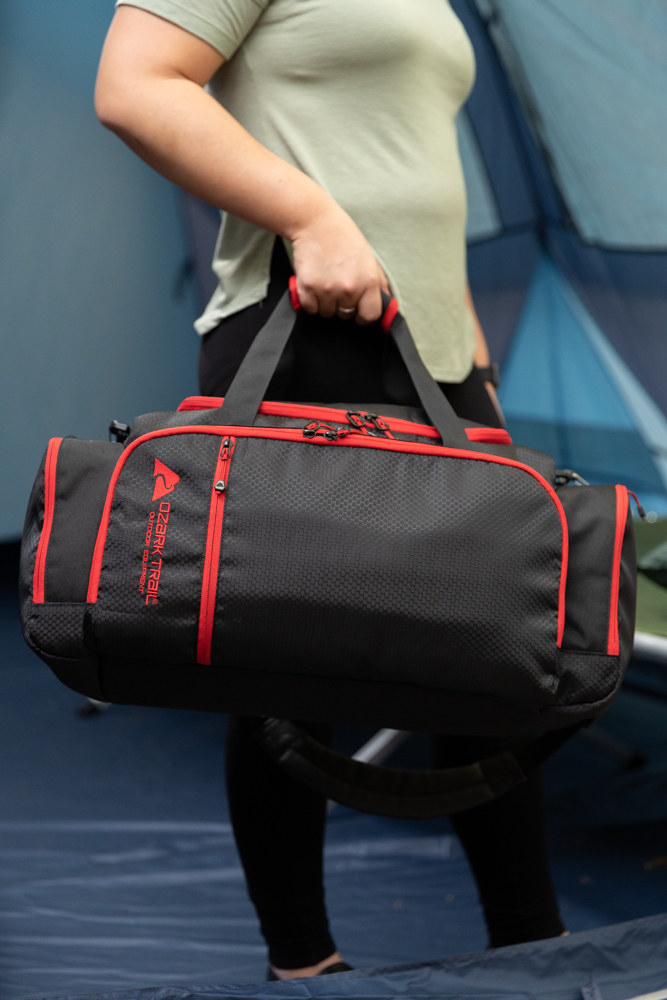 Model holding a black Ozark trail duffel bag with red trim