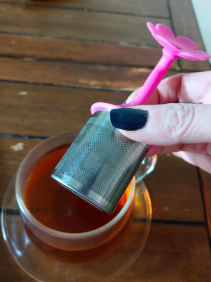 Reviewer holds pink floral and silver tea diffuser above a cup of brown tea