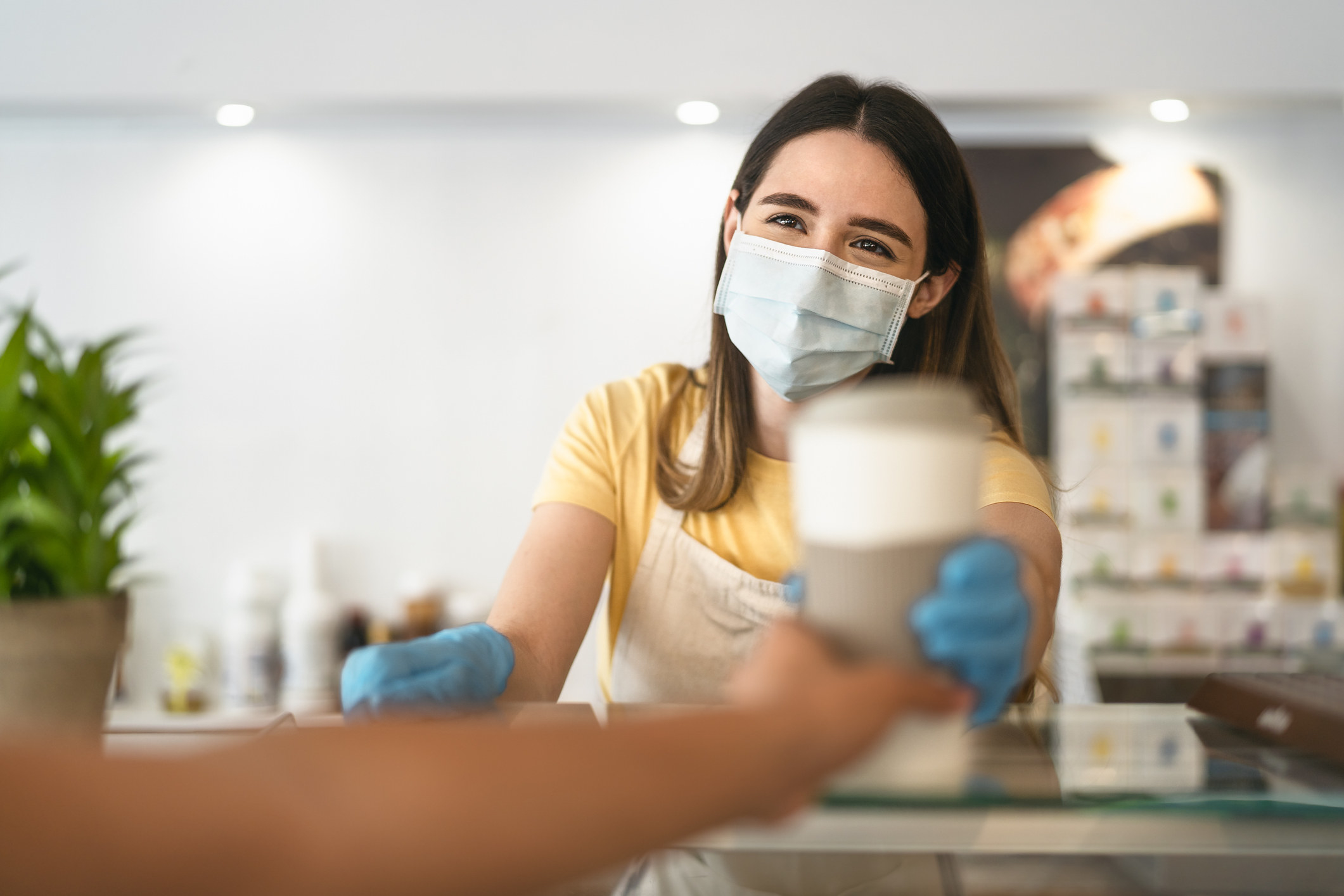 barista wearing mask handing cup of coffee to customer