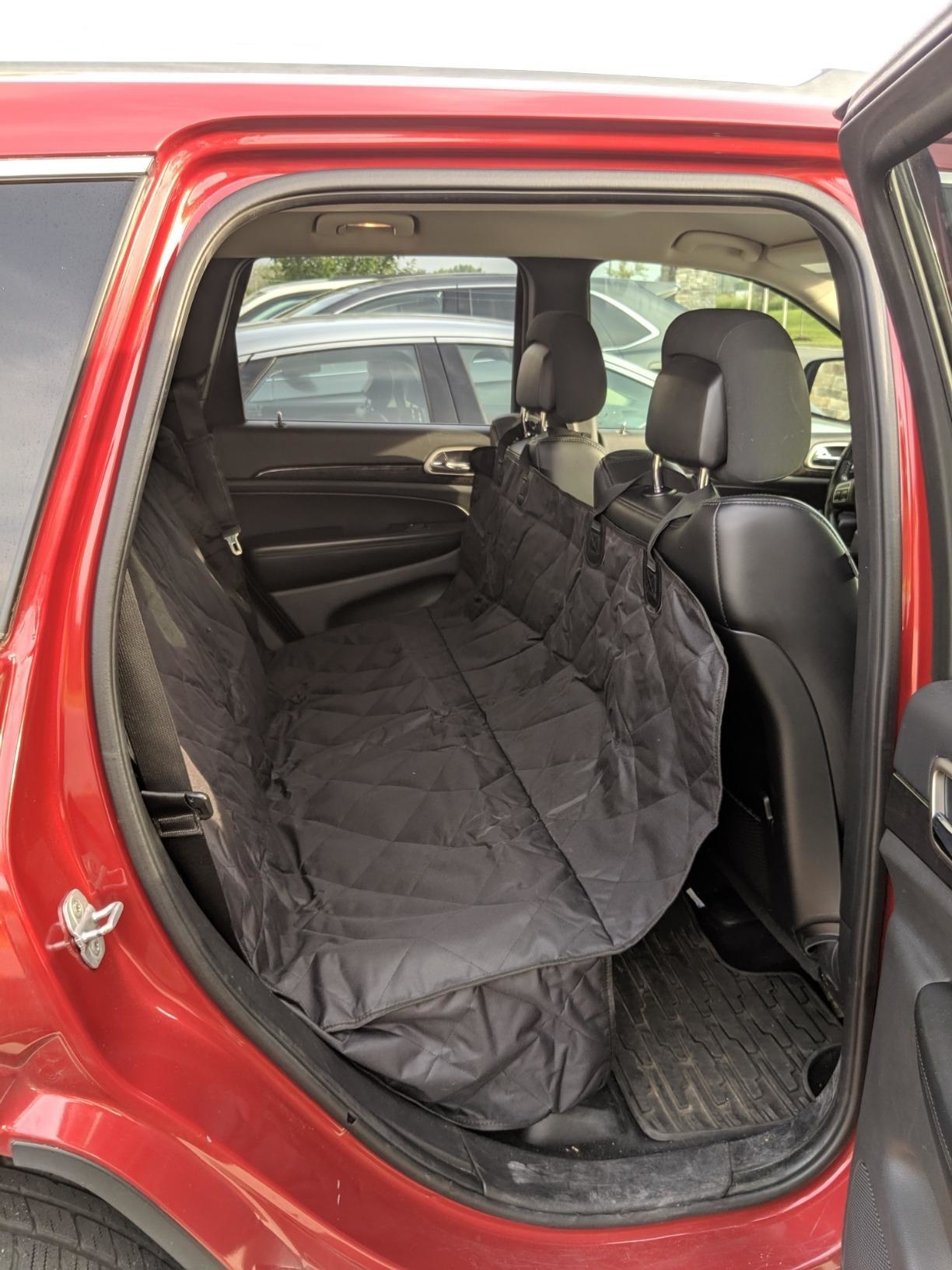 The cover in use in the backseat of a car, anchored to the headrests, creating a hammock that does not allow dog access to floor of car