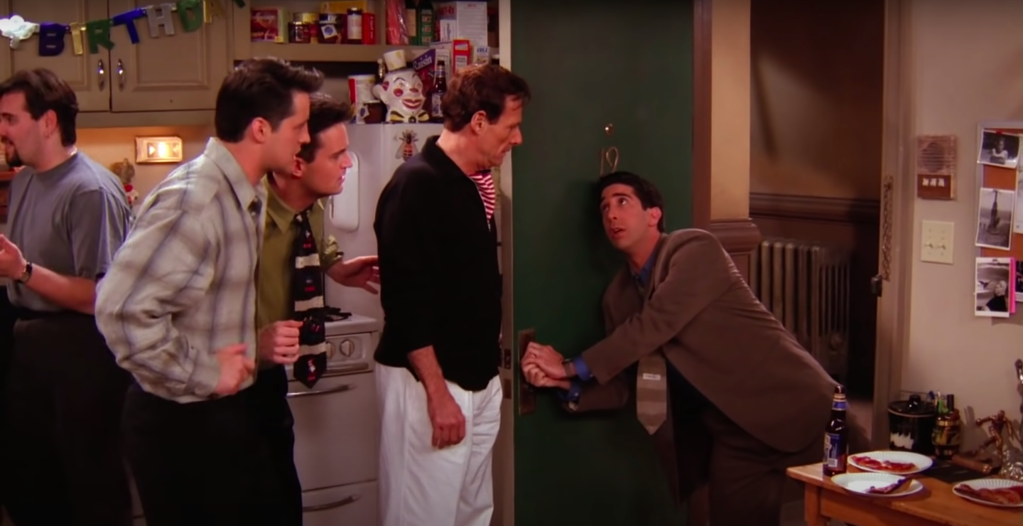 Ross is lunging and holding onto Chandler and Joey&#x27;s doorknob while Rachel&#x27;s dad, Chandler and Joey look at him