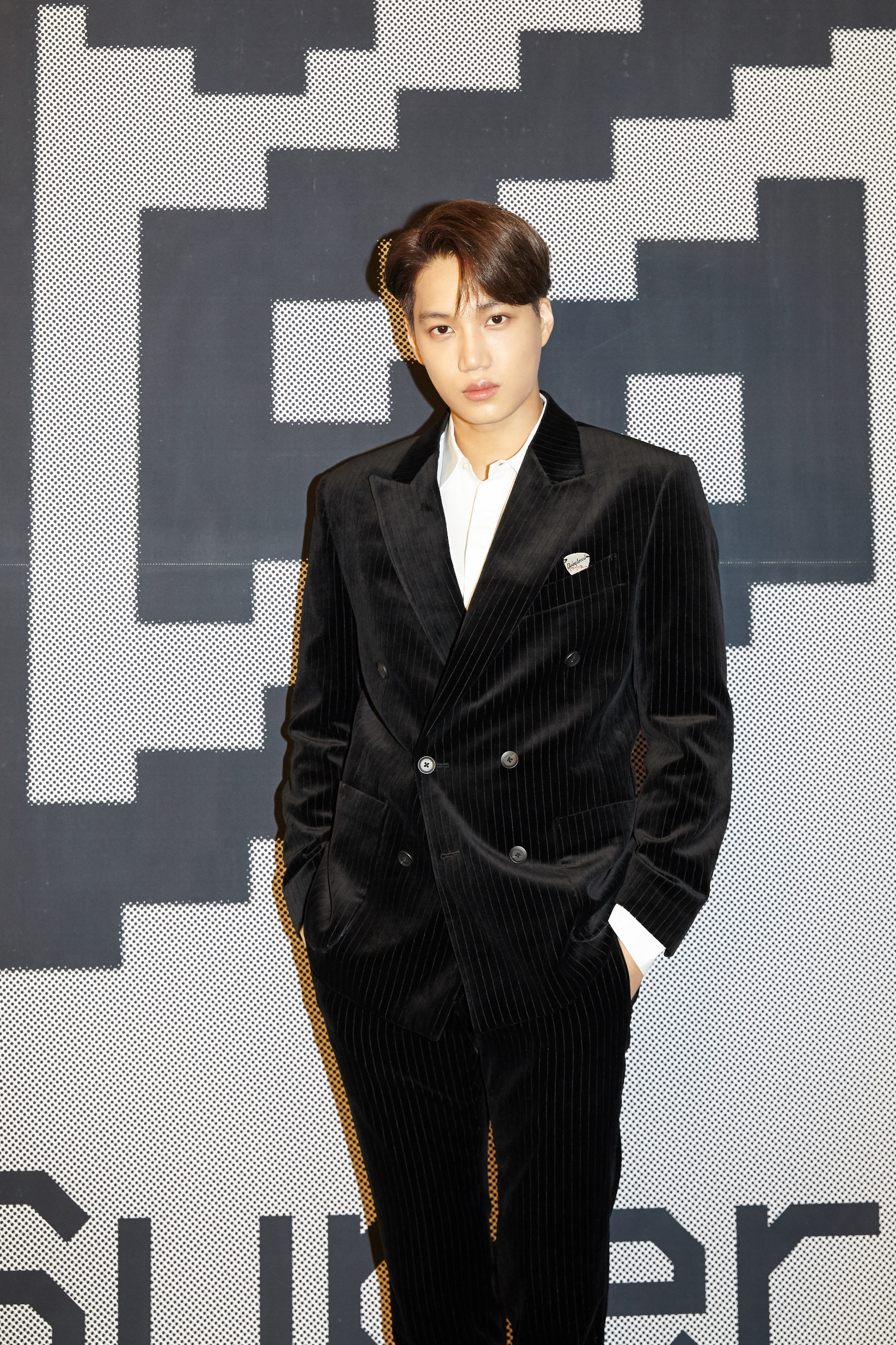 Kai stands with both hands in the pockets of his velvet pinstripe suit