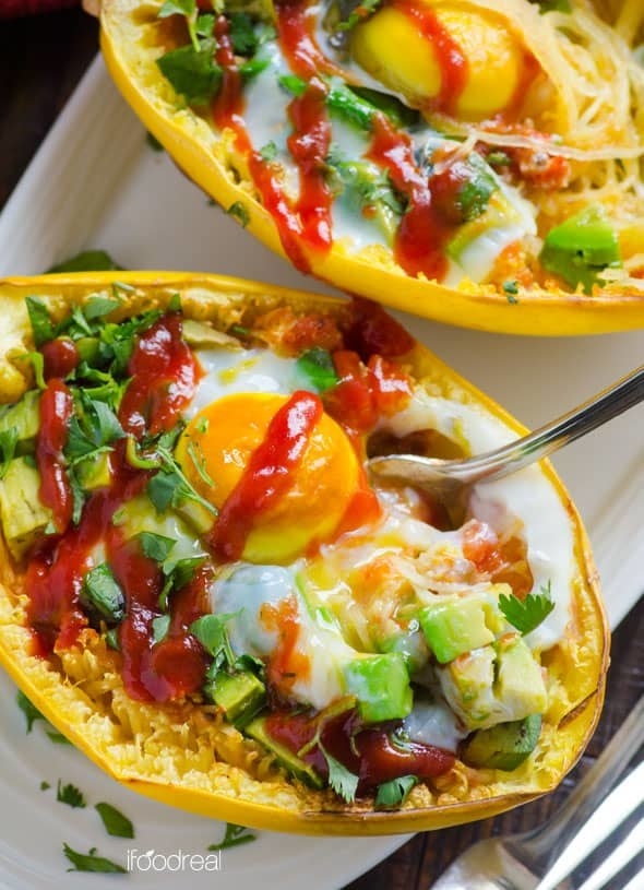 A halved spaghetti squash packed with salsa and sliced avocados, topped with a runny baked egg.