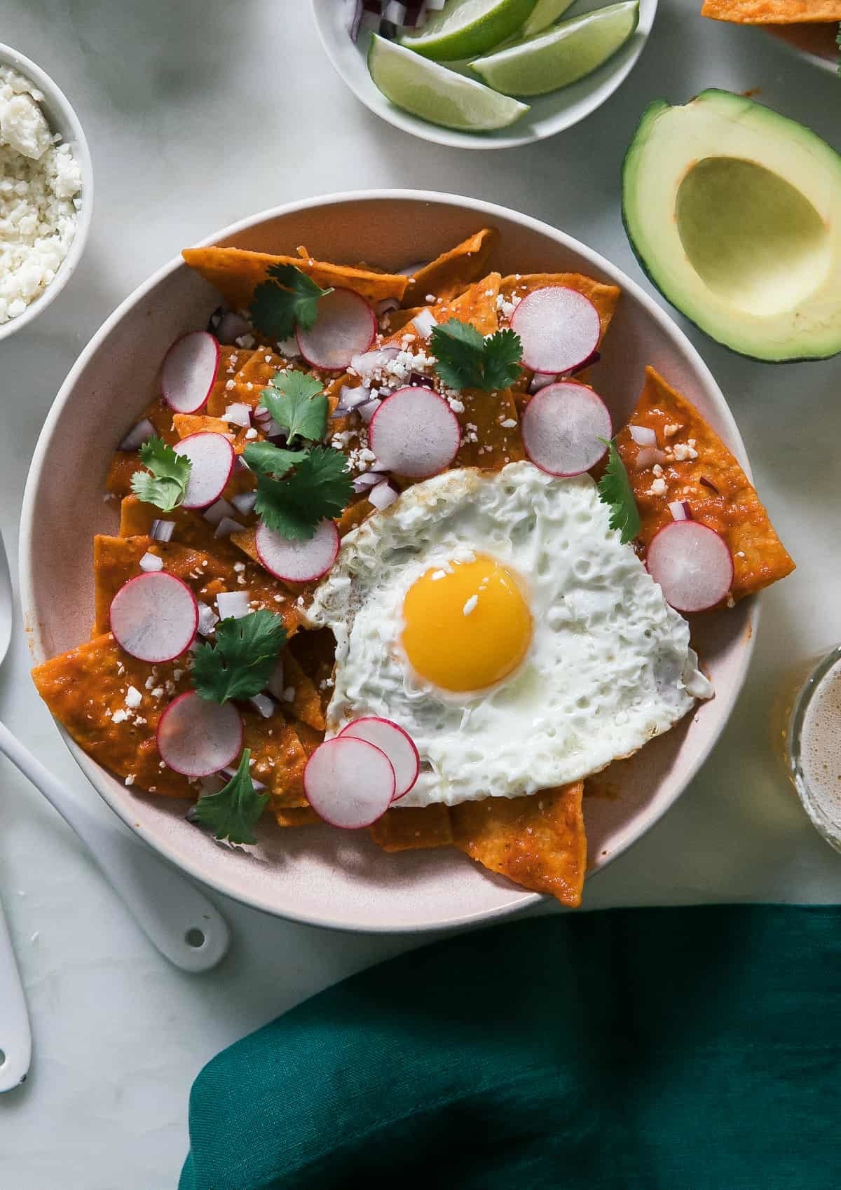 A plate covered in tortilla chips, which were tossed in a tomato sauce, topped with sliced radishes, cilantro, and a fried egg.