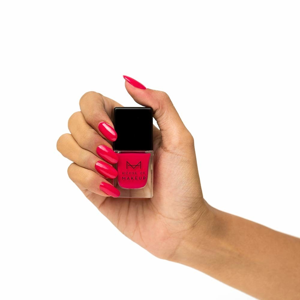 A hand holding up a cerise nail polish with the colour applied on the nails