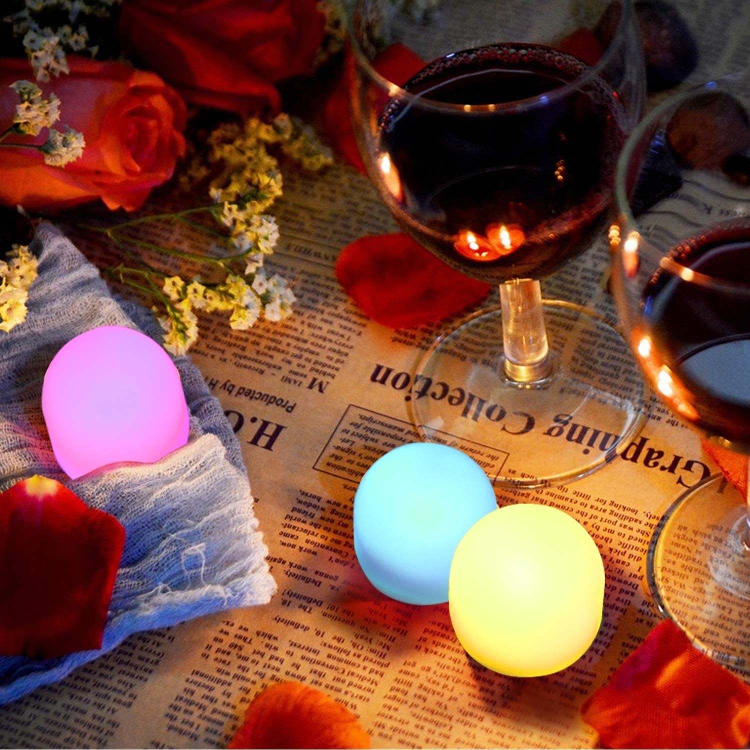 Three colourful nightlights illuminate a newspaper and wine glasses