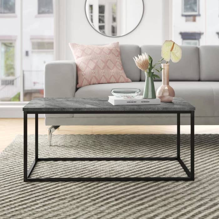The coffee table in black in front of a gray sofa with a pink pillow