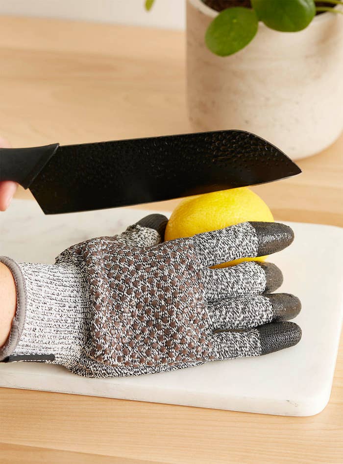 A person wearing a thick glove while cutting a lemon with a large knife