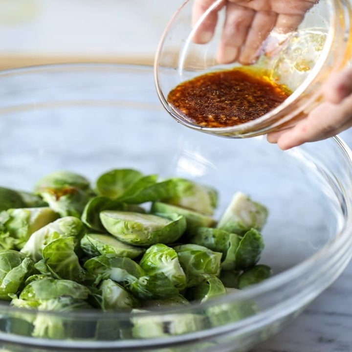 Pouring a honey garlic marinade onto a bowl of sliced Brussels sprouts.