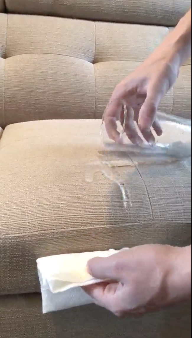 A reviewer pouring water on a couch, showing that it just slides down 