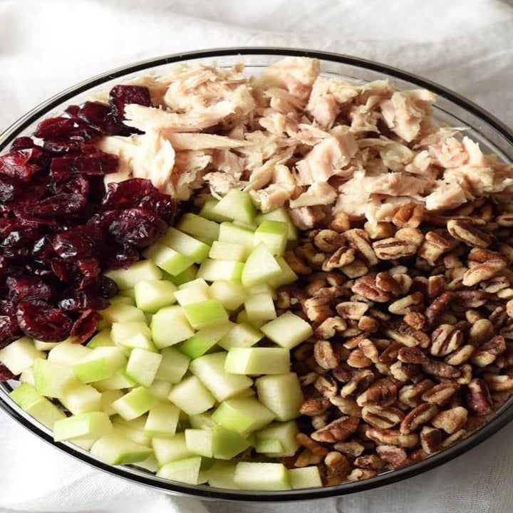 A bowl with cranberries, diced apples, pecans, and chicken.