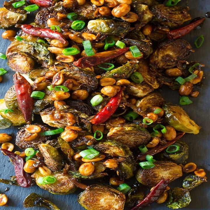 A plate of spicy roasted Brussels sprouts with chiles, roasted peanuts, and scallions.