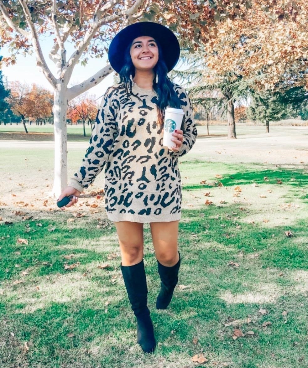 Reviewer wearing the tan mid-thigh length sweater with black leopard print as a dress with knee-high boots