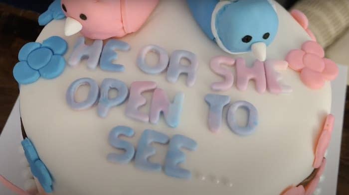 A gender-reveal cake with the words &quot;He or she, open to see&quot; in blue and pink icing