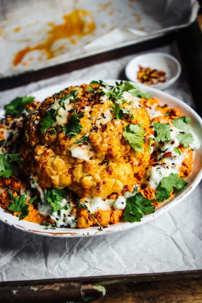 A whole roasted cauliflower topped with fresh herbs and creamy cucumber sauce.