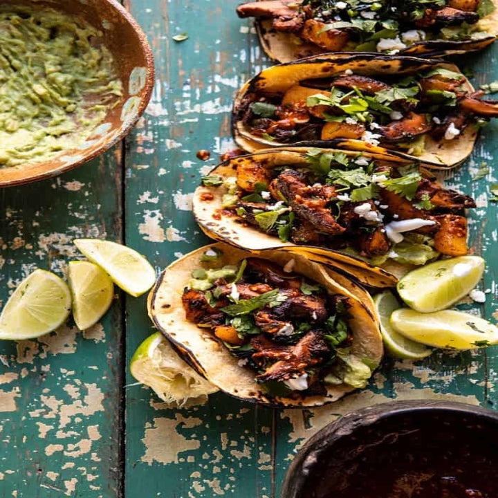 Four mushroom tacos with guacamole and lime wedges on the side.