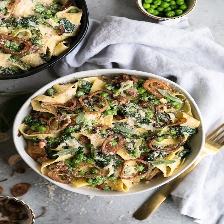 A bowl of pasta with spinach, peas, and crispy shallots.