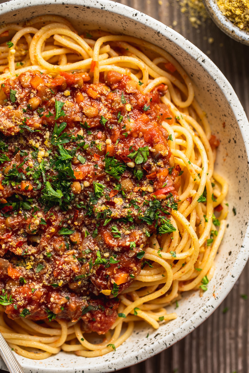A bowl of pasta topped with vegetarian Bolognese sauce and fresh herbs.