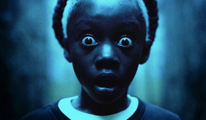 A young girl has a braid going across the top of her head. She is in a dark room, and her eyes and mouth are as wide as possible