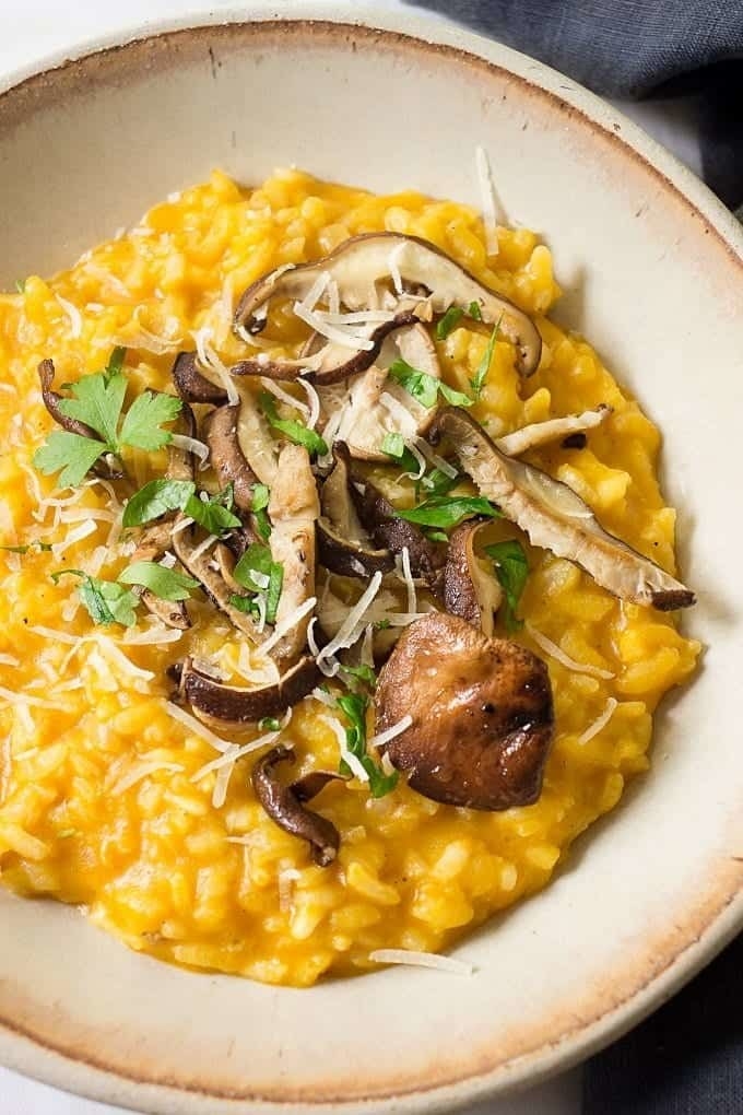 A bowl of pumpkin risotto topped with roasted sliced mushrooms, Parmesan cheese, and fresh herbs.