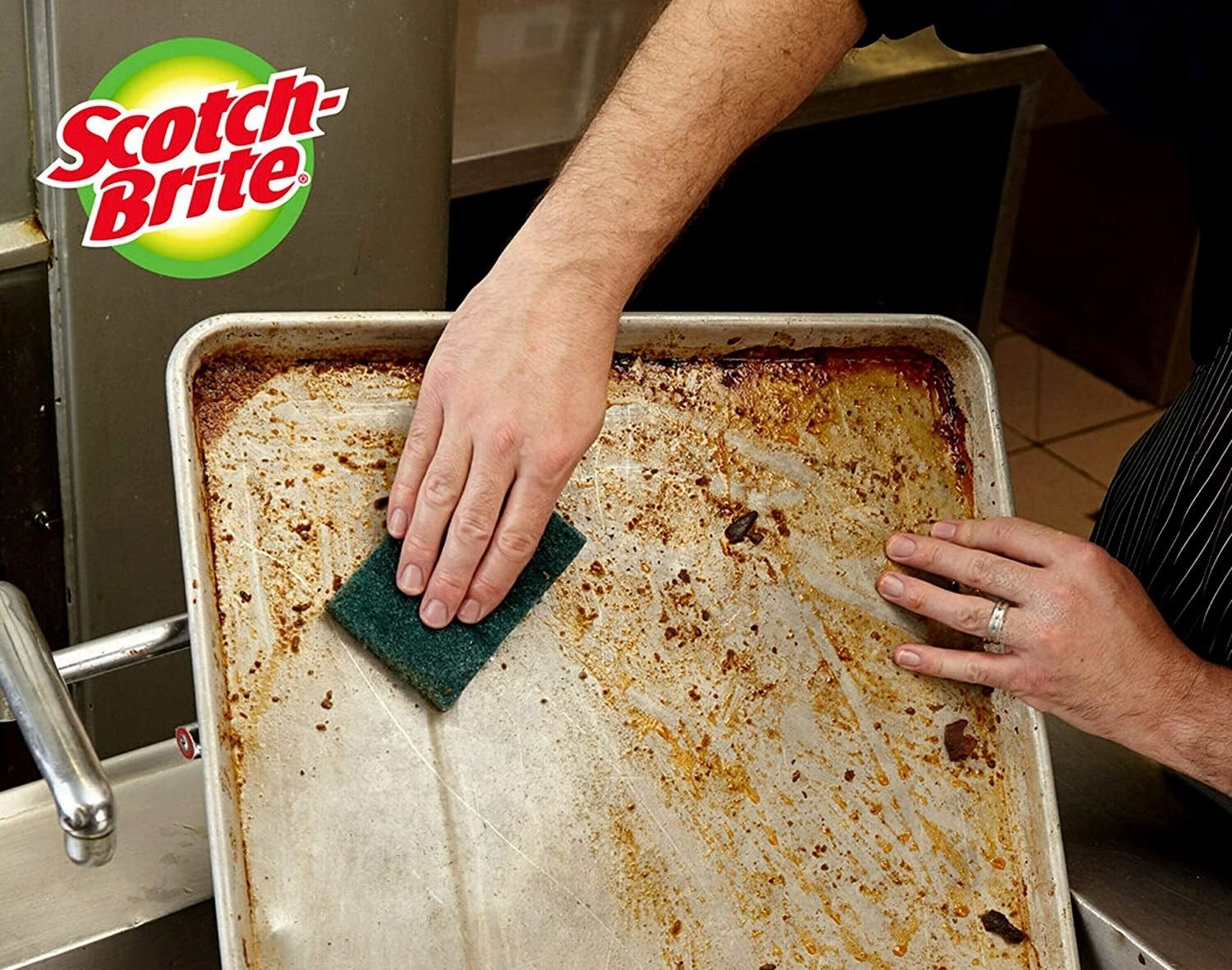 the green scrubbing pad being used on a dirty baking sheet