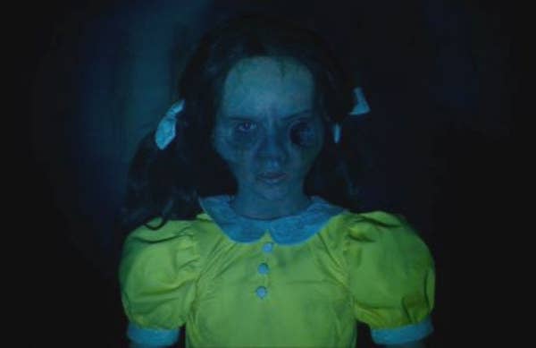 A girl with two pigtails is staring at the camera while wearing a dress with buttons and a peter pan collar