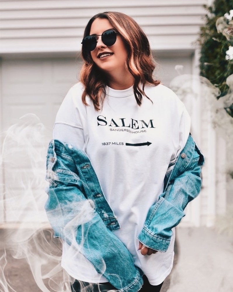 a model wearing a white oversized tee with the words &quot;salem sanderson home 1837 miles&quot; on it in black