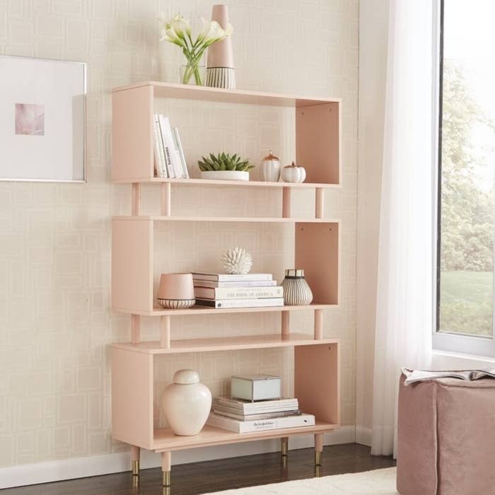 a pink bookshelf with three big shelves, two smaller shelves between them, and gold legs
