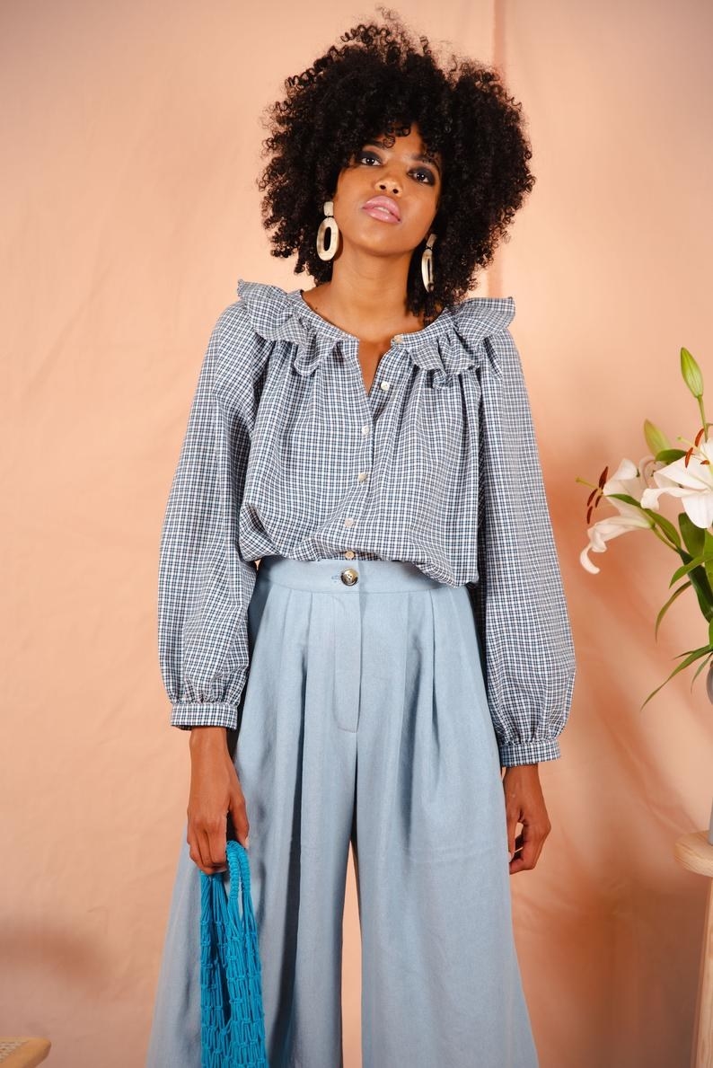 Model wearing the wrist-length blue plaid shirt with white buttons down the front and a ruffled collar.