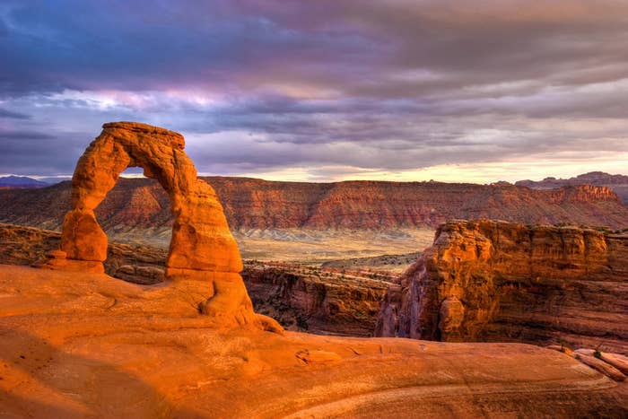 Natural red rock arch perched above giant plateaus captured at sunset as a storm is rolling in