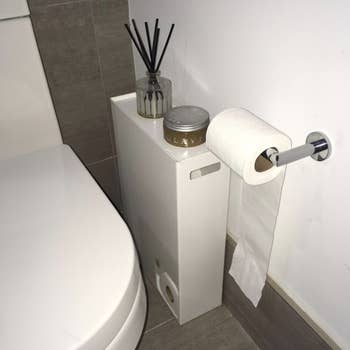A toilet paper stocker in a bathroom between the wall and toilet