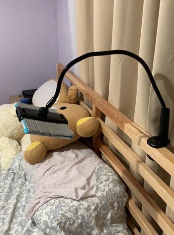 Reviewer photo of the stand in black clipped to the bedframe and holding an iPad above a pillow