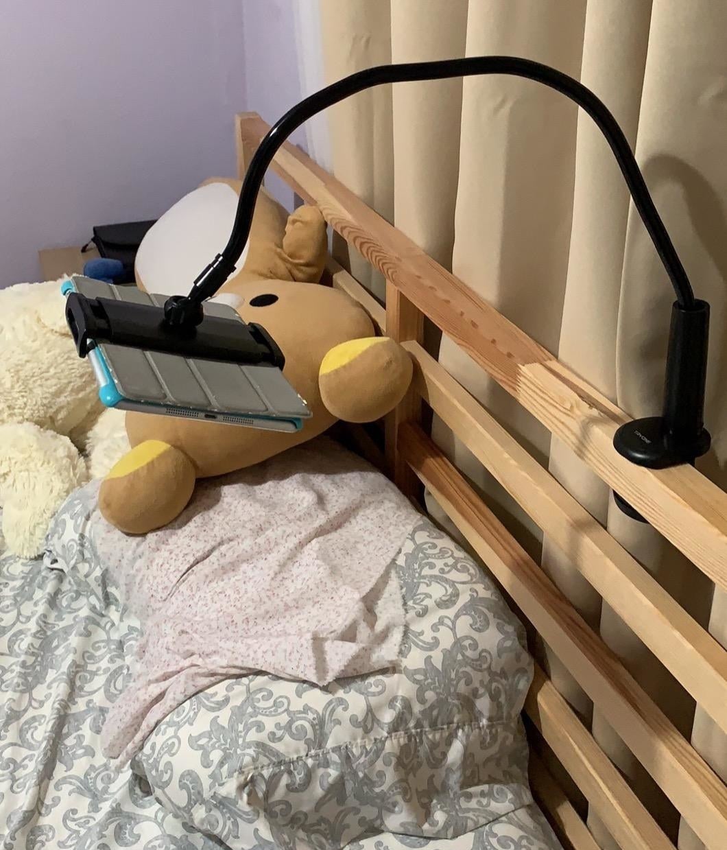 Reviewer photo of the stand in black clipped to the bedframe and holding an iPad above a pillow