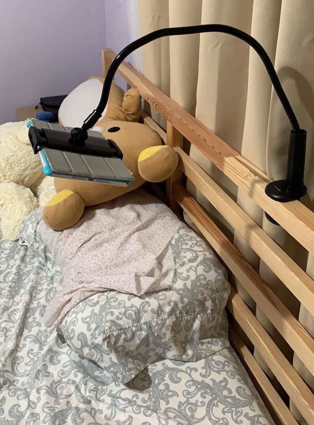 Reviewer photo of the stand in black clipped to the bedframe and holding an iPad above a pillow