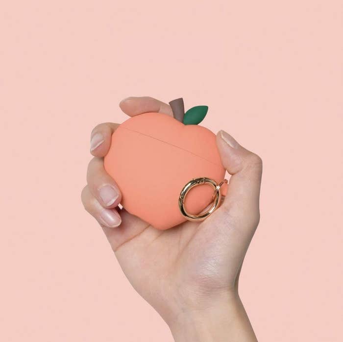 A person holds the peach-shaped ear pod case against a colourful background