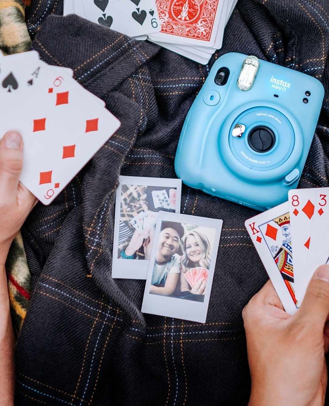 A Fujifilm camera on a cloth with two pictures and playing cards