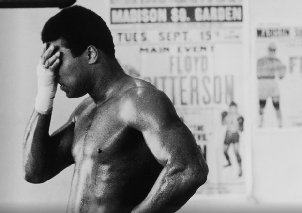 black and white photo of Muhammad Ali shirtless with his right hand on his forehead