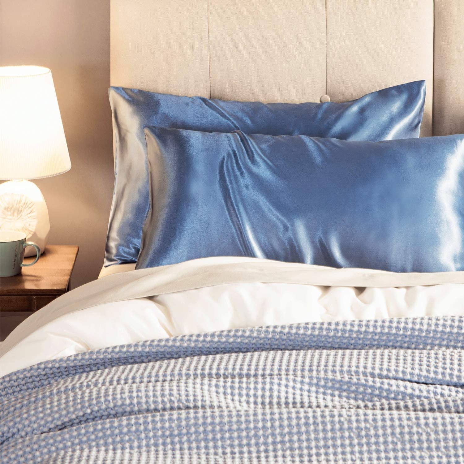 Two blue satin pillowcases on pillows and styled on a bed