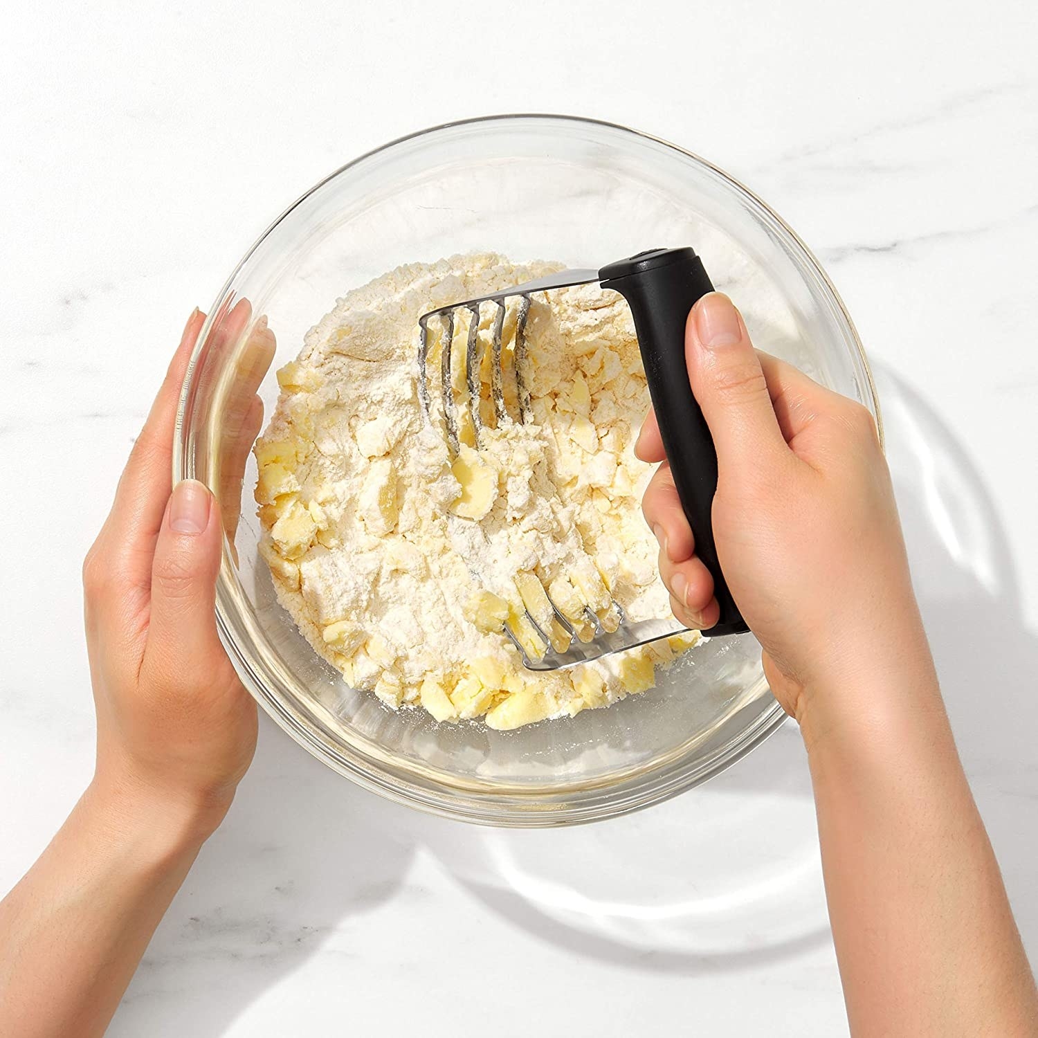 A person kneads butter into a bowl full of flour