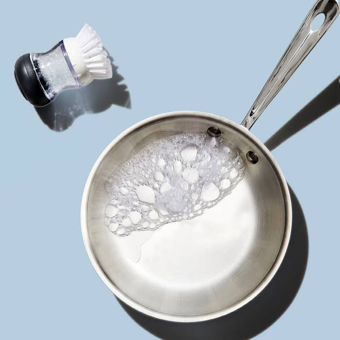 An overhead photo of a soapy metal pan with the scrubbing brush next to it