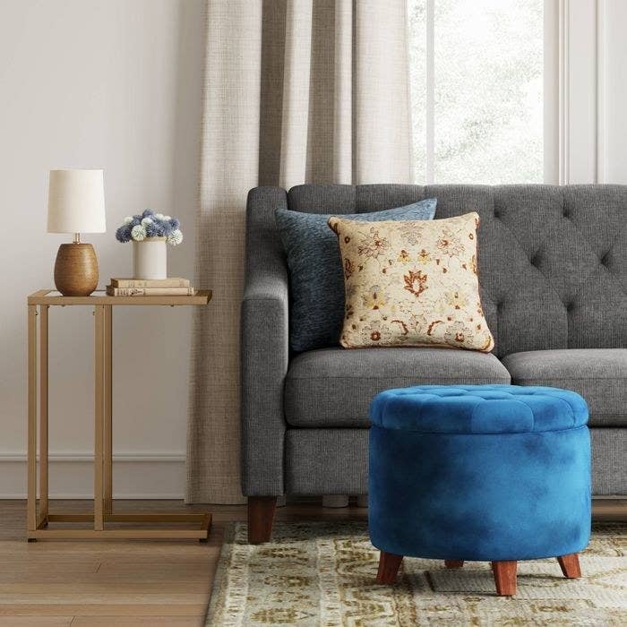 The velvet navy Threshold Tufted Round Storage Ottoman in a living room