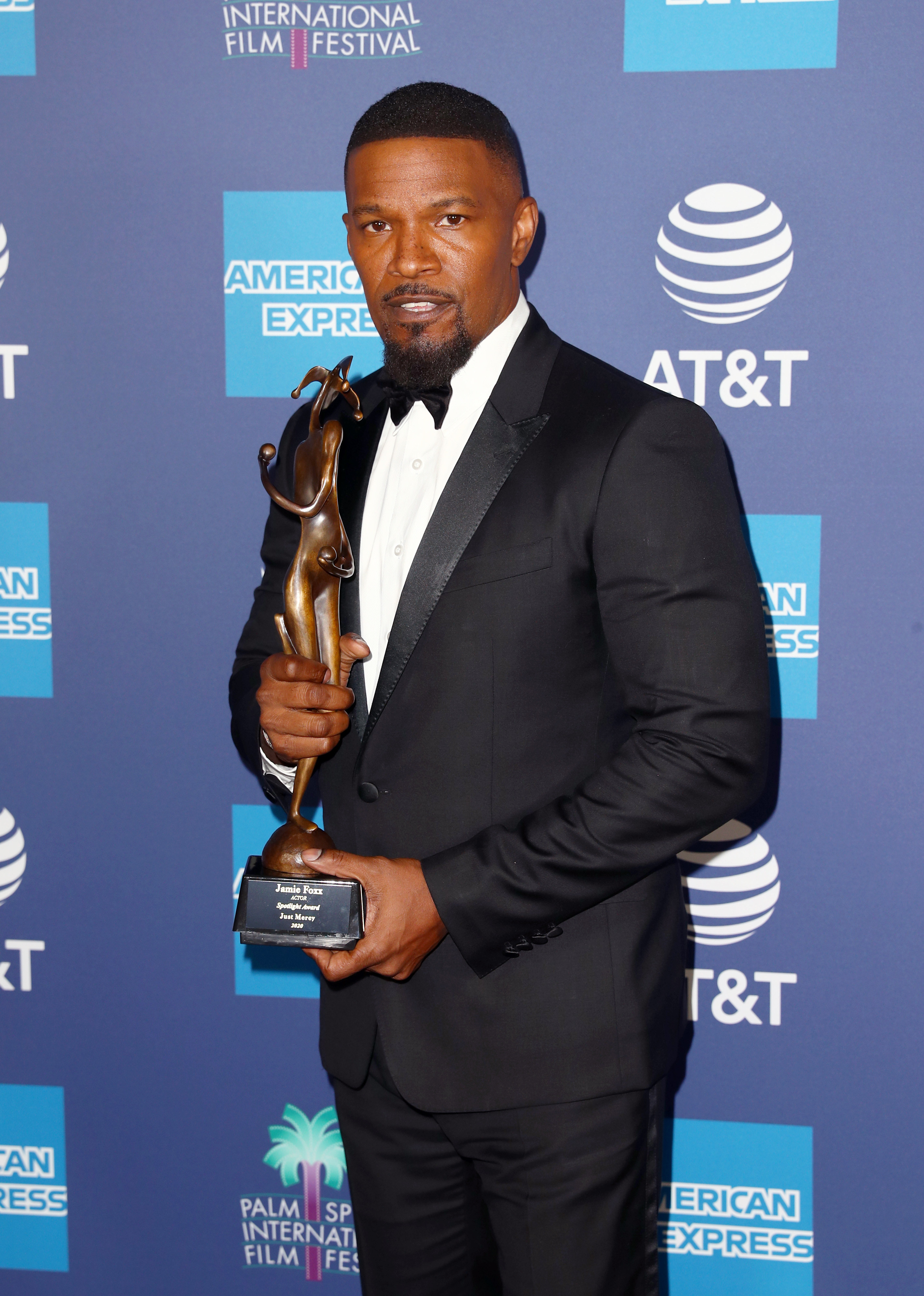 Jamie Foxx holding an award wearing a dark suit and bright shirt