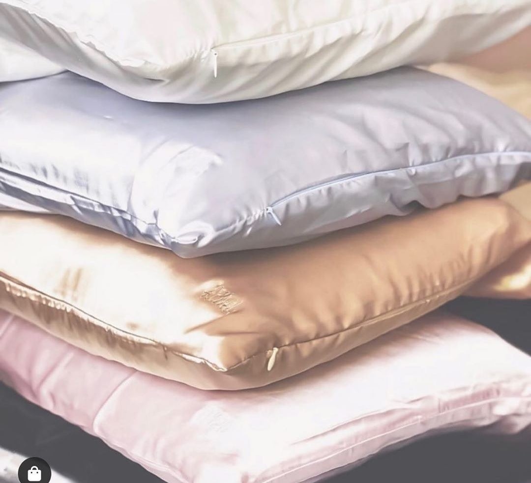 Four pillows with silk pillowcases sitting on top of each other in white, grey, gold, and pink.  