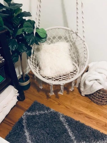Reviewer pic of the circular macrame hammock chair hanging from the ceiling in the corner of the room. 