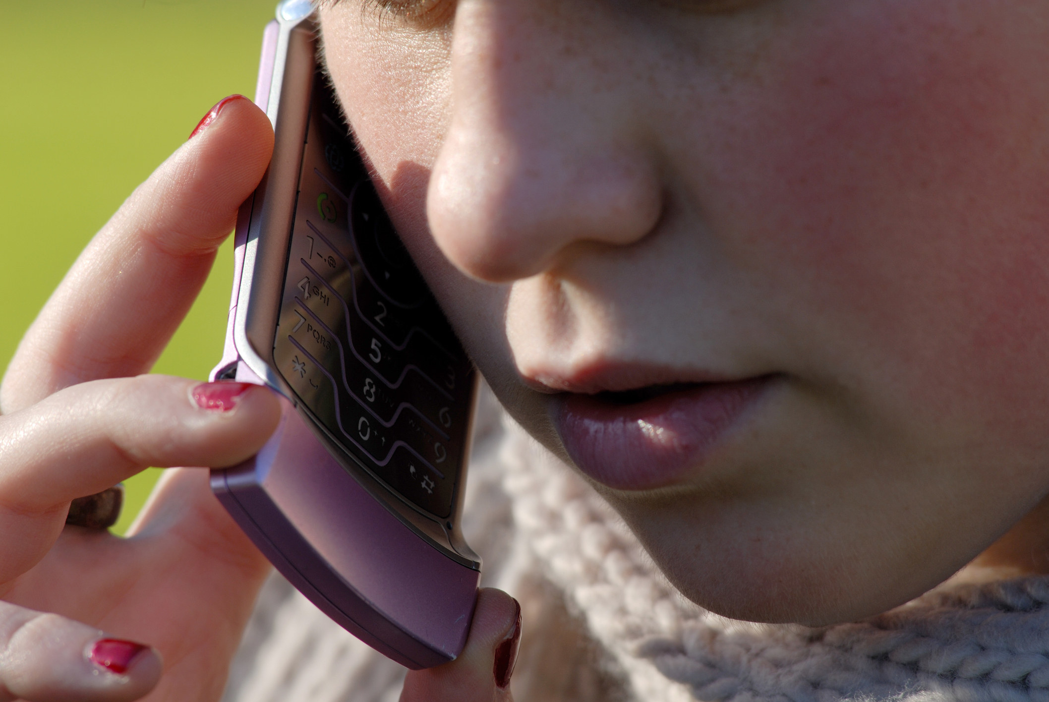 A stock image of a close-up of a teen girl talking on a hot pink Razr phone