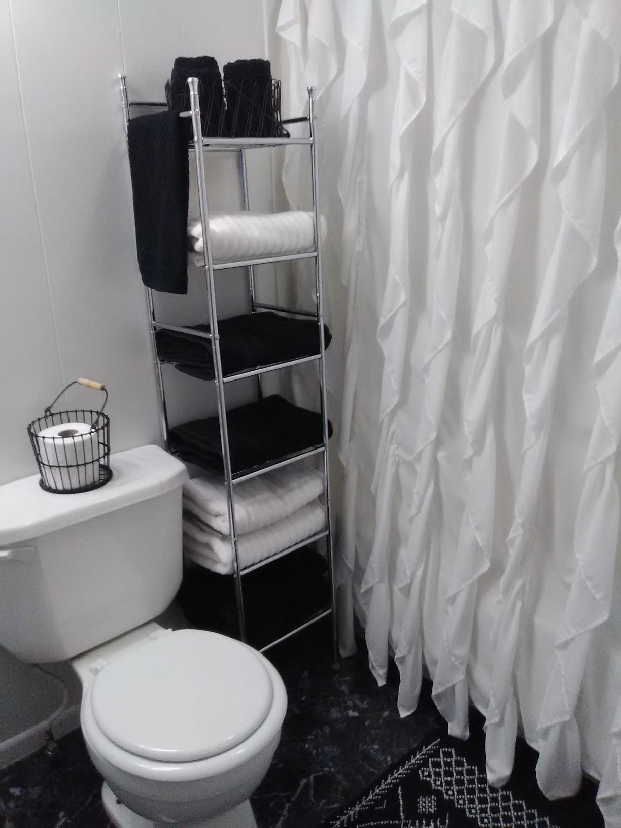 Reviewer pic of the six-shelf rack between a toilet and shower with towels on each shelf