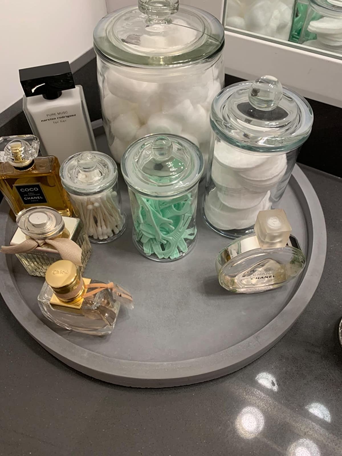 Reviewer pic of the grey stone tray with an outer lip on a table with assorted bathroom products and perfume bottles on it