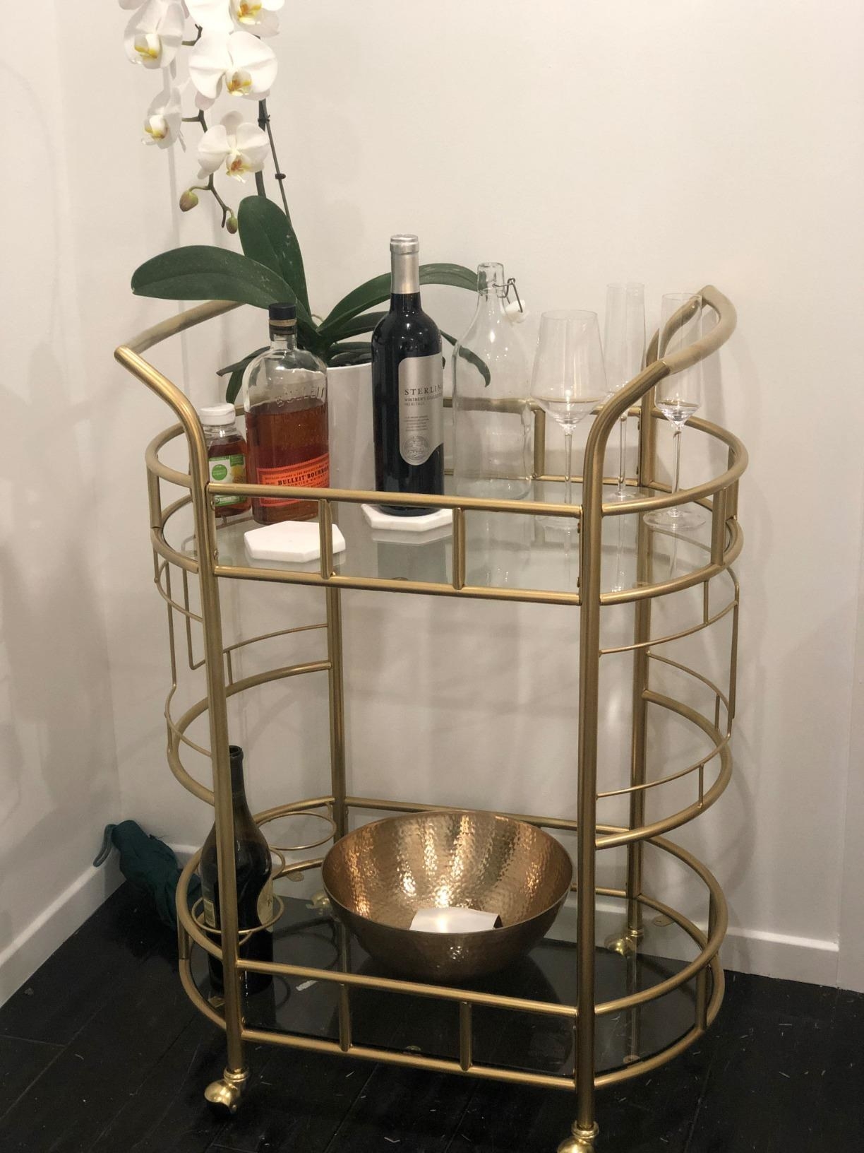 Reviewer pic of the oval-shaped bar cart in gold with assorted drinks and glasses on it