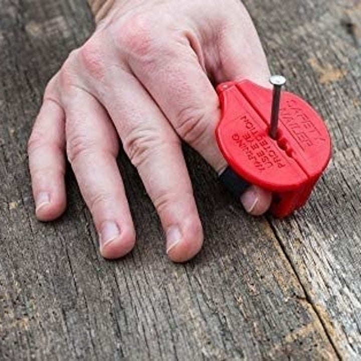 A hand with the small red gadget pinched between thumb and pointer finger